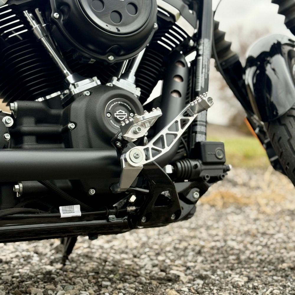 The TC Bros. Pro Series Truss Brake Arm is a 6061-T6 aluminum upgrade for 2018-up Harley-Davidson Softail brake pedals, featuring triangular cutouts and a circular mounting hole—available in silver or black.