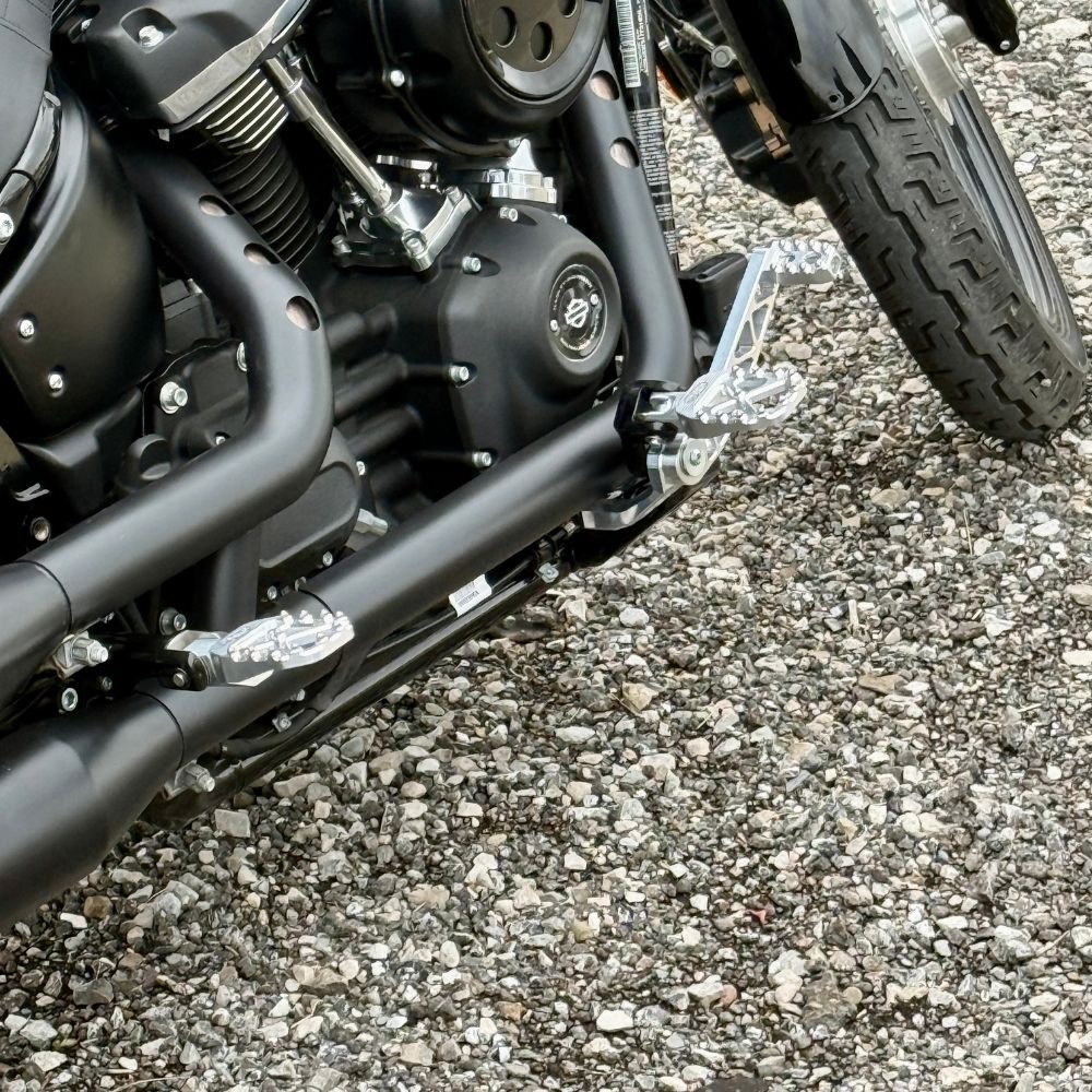 The TC Bros. Pro Series Truss Brake Arm is a 6061-T6 aluminum upgrade for 2018-up Harley-Davidson Softail brake pedals, featuring triangular cutouts and a circular mounting hole—available in silver or black.