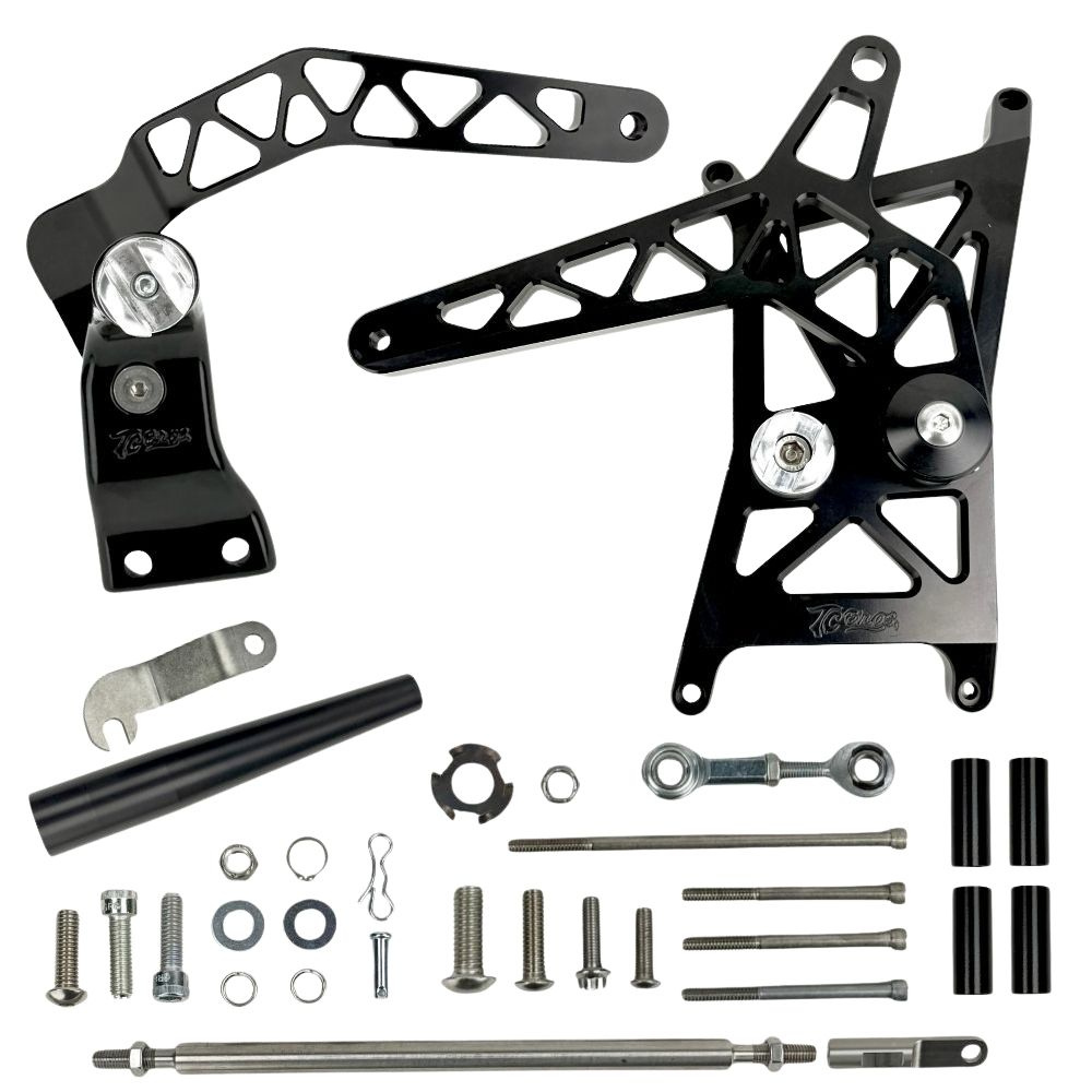 A collection of assorted metal rearset components—including brackets, bolts, rods, washers, spacers, and foot pegs—by TC Bros., displayed on a white background. These parts are designed for compatibility with the TC Bros. Pro Series Mid Controls for 2006–2017 Harley-Davidson Dyna motorcycles.