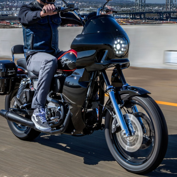 A Saddlemen Mini Fairing in black, specifically for 1996-2005 Dyna Models, featuring a large circular cutout for headlight fitting and a small rectangular side vent designed to enhance wind protection.