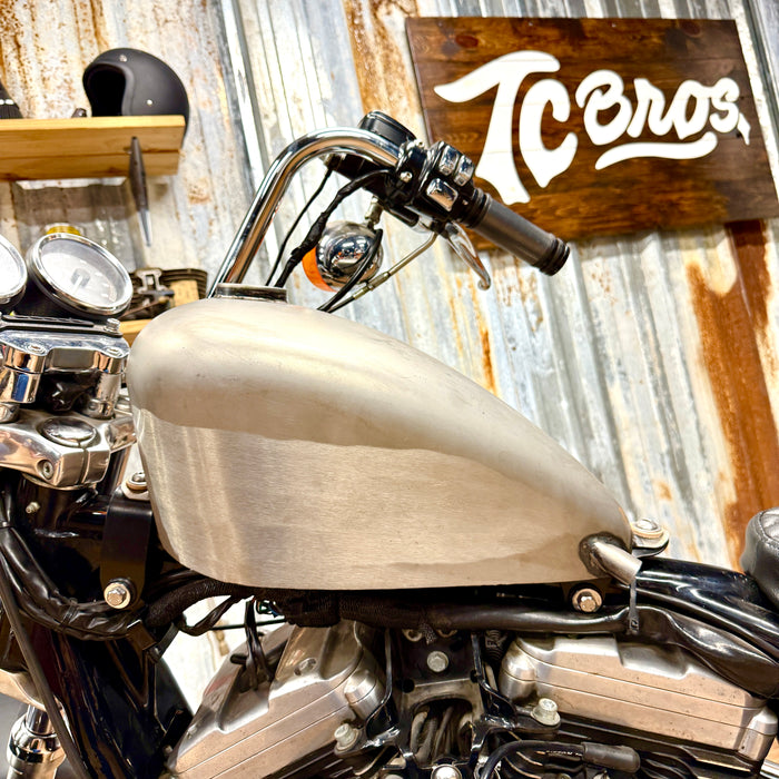 The TC Bros. Frisco Gas Tank Adapter Brackets set for 1982-2003 Harley-Davidson Sportster includes black metal brackets, bolts, washers, nuts, and rubber grommets—perfect for tongue-mount fuel tank installations.