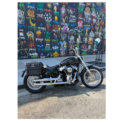 Two black, waterproof Speedwell Vigilante Saddlebags - Harley M8 Softail (with tail light/turn signal kit) with handles, one open and one closed, displayed against a white background.