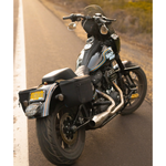 A man stands by his bike with the Throttle Twist Hybrid Saddlebag/Backpack—versatile motorcycle luggage that easily converts into a backpack. Text: "Convertible Saddlebags/Backpack." Brand: Throttle Twist.