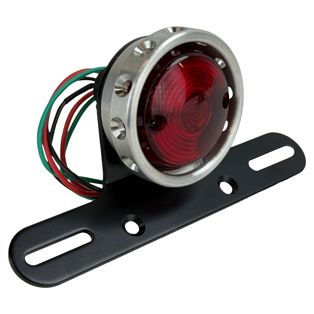 The Mid-USA Vintage Drilled Tail Light by Mid-USA features a round red lens in an aluminum housing, mounted on a black bracket with exposed electrical wires at the back.