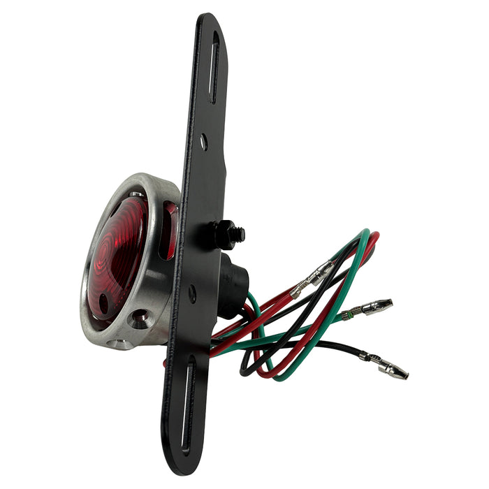 The Mid-USA Vintage Drilled Tail Light by Mid-USA features a round red lens in an aluminum housing, mounted on a black bracket with exposed electrical wires at the back.