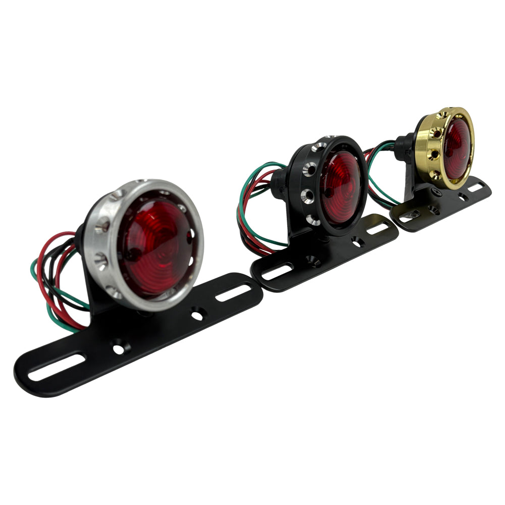 The Mid-USA Vintage Drilled Tail Light by Mid-USA features a round red lens in an aluminum housing, mounted on a black bracket with exposed electrical wires at the back.