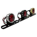 The Mid-USA Vintage Drilled Tail Light by Mid-USA features a round red lens in an aluminum housing, mounted on a black bracket with exposed electrical wires at the back.