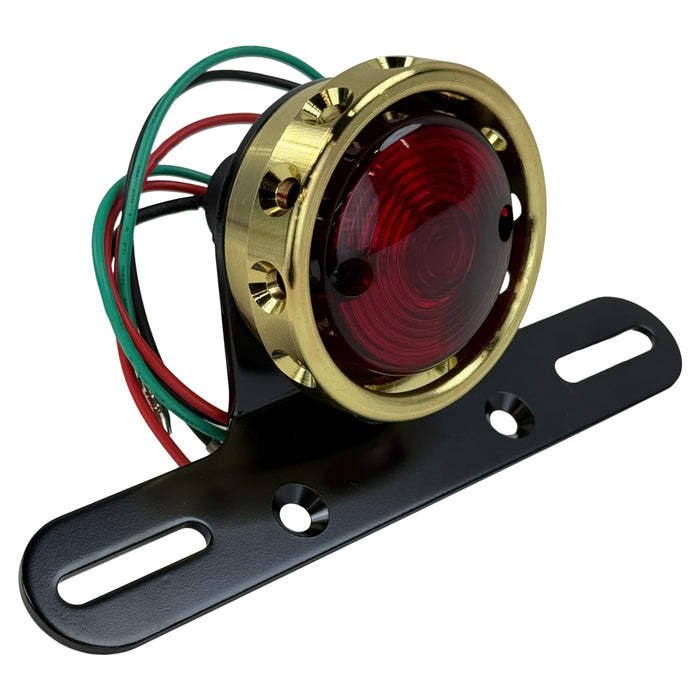 The Mid-USA Vintage Drilled Tail Light by Mid-USA features a round red lens in an aluminum housing, mounted on a black bracket with exposed electrical wires at the back.