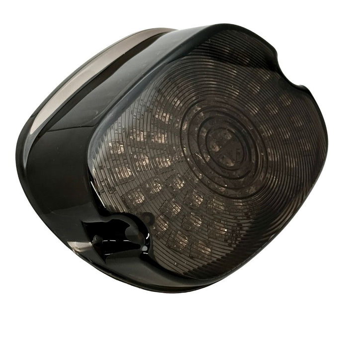 A close-up of the Moto Iron® LED Laydown Squareback Light for 1973-2024 Harley-Davidson, showcasing its dark, rounded design with a smoked lens and integrated turn signals.