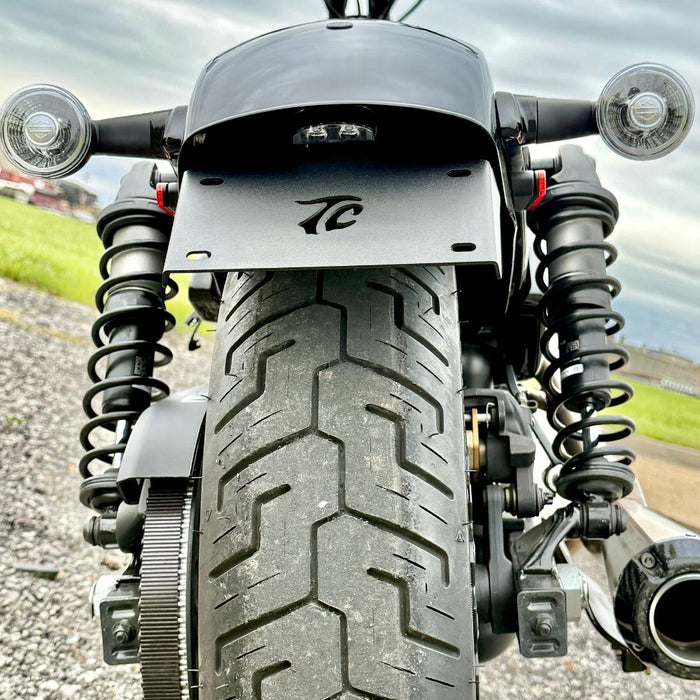 TC Bros. License Plate Relocation Bracket for 2022-Up Harley-Davidson Nightster RH975, with logo, includes screws, washers, nuts, bolt, and a black rectangular piece—all neatly arranged on a white background.