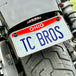 TC Bros. License Plate Relocation Bracket for 2022-Up Harley-Davidson Nightster RH975, with logo, includes screws, washers, nuts, bolt, and a black rectangular piece—all neatly arranged on a white background.