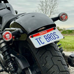 TC Bros. License Plate Relocation Bracket for 2022-Up Harley-Davidson Nightster RH975, with logo, includes screws, washers, nuts, bolt, and a black rectangular piece—all neatly arranged on a white background.