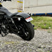 TC Bros. License Plate Relocation Bracket for 2022-Up Harley-Davidson Nightster RH975, with logo, includes screws, washers, nuts, bolt, and a black rectangular piece—all neatly arranged on a white background.