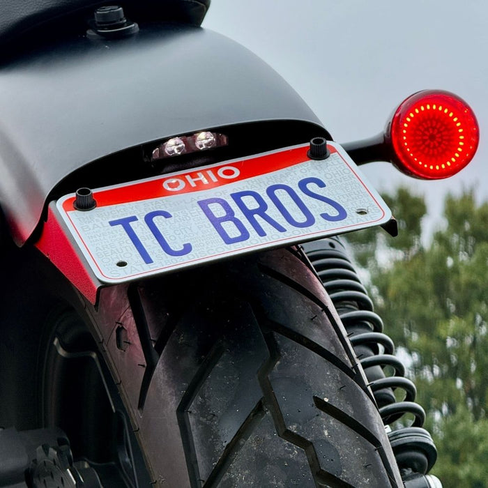 Black metal TC Bros. License Plate Relocation Bracket for 2010-2022 Harley-Davidson Sportster with mounting hardware for saddlebag installation.