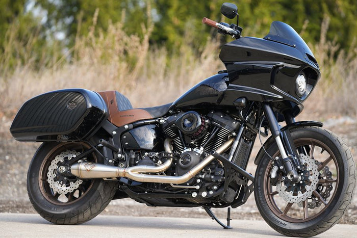 SP Concepts Big Bore Exhaust M8 Softail ST & Sport Glide (TC Bros. Mids) 2018-Present headers and performance exhaust system on a concrete floor with a part of a helmet featuring an American flag design in the background.