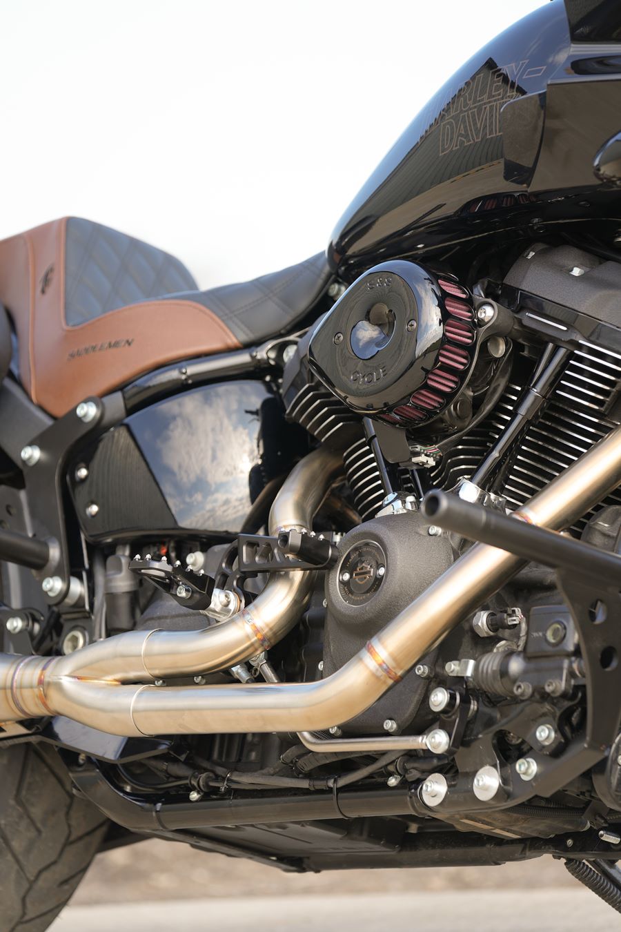 An SP Concepts Lane Splitter Exhaust M8 Softail ST & Sport Glide (TC Bros. Mids) 2018-Present sits on a workshop surface with an American flag design visible in the background.