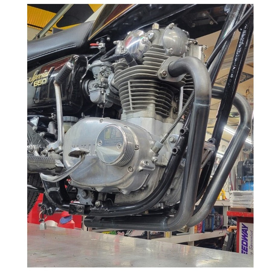 Close-up view of a motorcycle engine and Pandemonium Hustler XS650 exhaust system in a workshop setting.