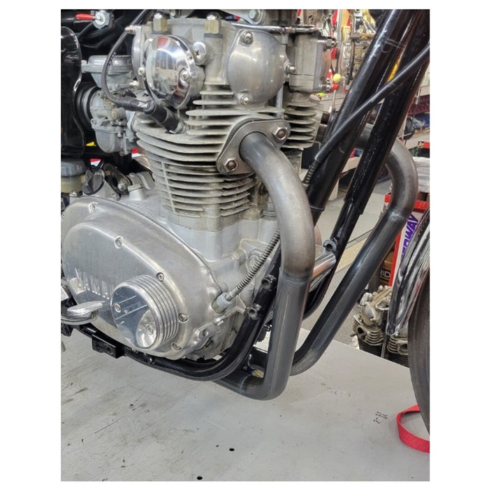 Close-up view of a motorcycle engine and Pandemonium Hustler XS650 exhaust system in a workshop setting.