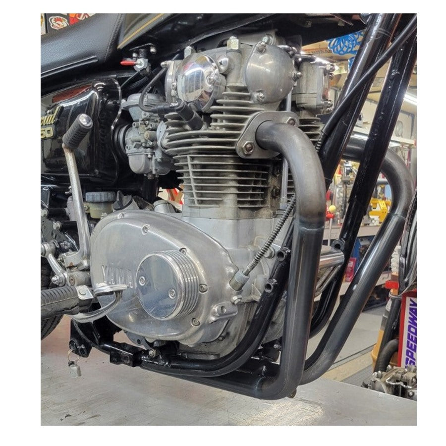 Close-up view of a motorcycle engine and Pandemonium Hustler XS650 exhaust system in a workshop setting.