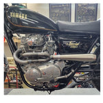 A side view of a Yamaha XS650 motorcycle's Pandemonium 2 into 1 XS650 exhaust system in a workshop setting.