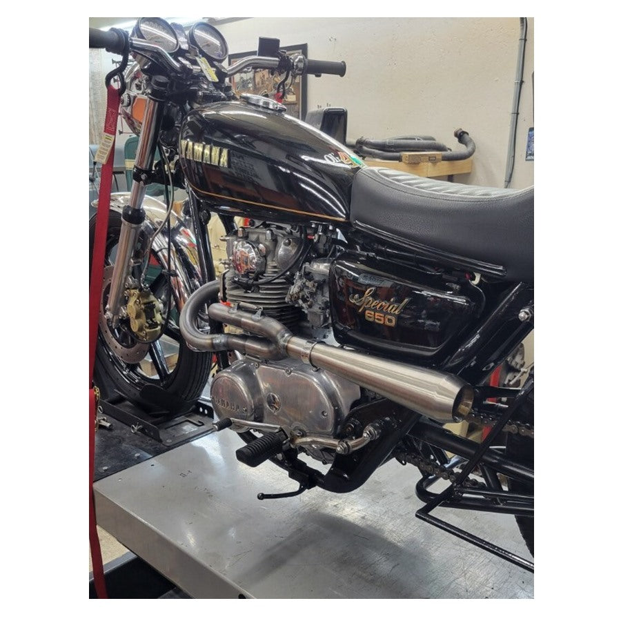 A side view of a Yamaha XS650 motorcycle's Pandemonium 2 into 1 XS650 exhaust system in a workshop setting.