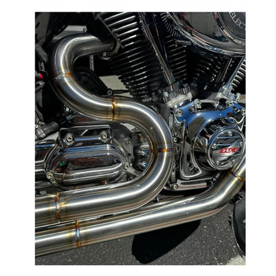 A red motorcycle parked outside a garage, equipped with SP Concepts' gleaming stainless steel TC Bagger Full Length Turnpike Exhaust for 1995-2016 Touring models, sits next to metal racks. Inside, an American flag hangs proudly amidst tools and parts for these touring models.