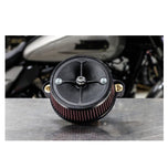 Close-up of a black circular mechanical component with a central screw and four spokes, two metal mounting brackets, and a red ribbed filter around its perimeter, resembling the Stealth Air Cleaner Kit - Black Cover - For 23 CVO Road Glide & 24+ Touring often seen on Road Glide models by S&S Cycle.