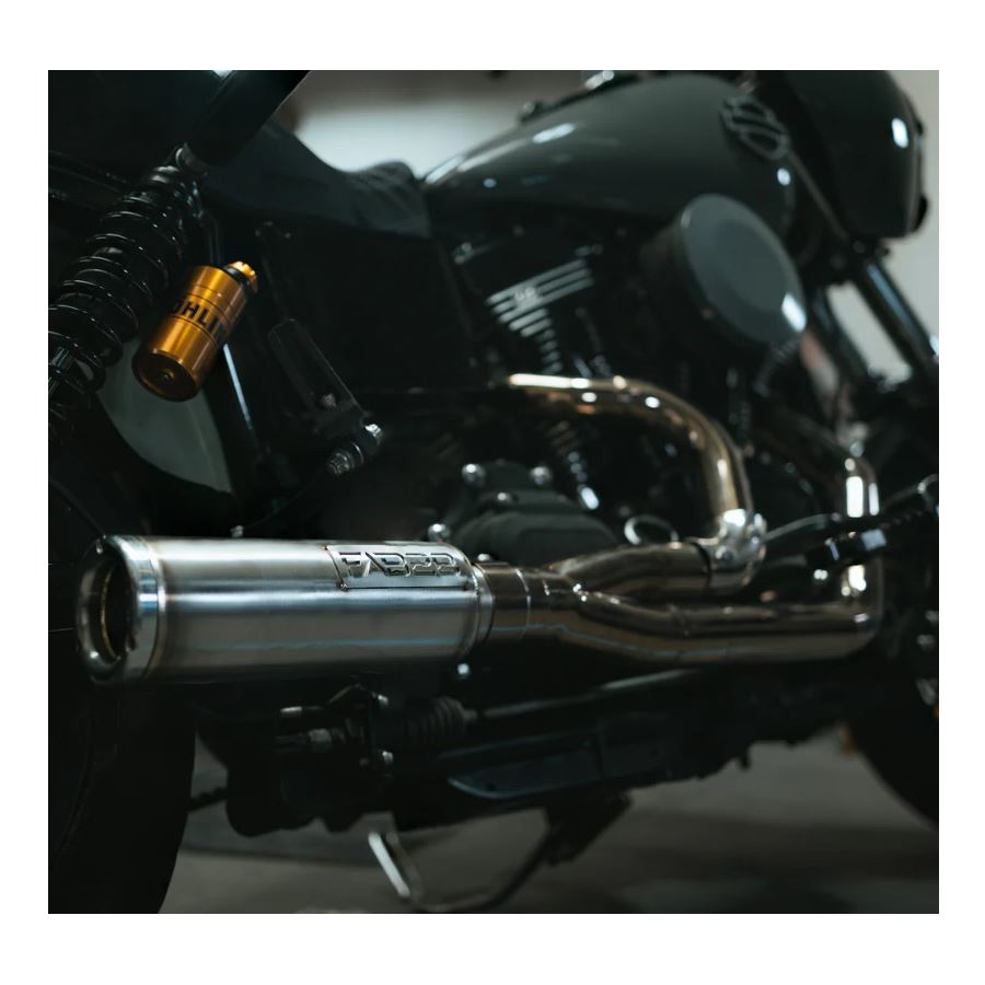 The Fab 28 Stainless Exhaust with Canister Muffler for '99-'17 Dyna Models is showcased on a wooden platform adorned with a carved American flag and a dragon design, making it an ideal choice for your bike.