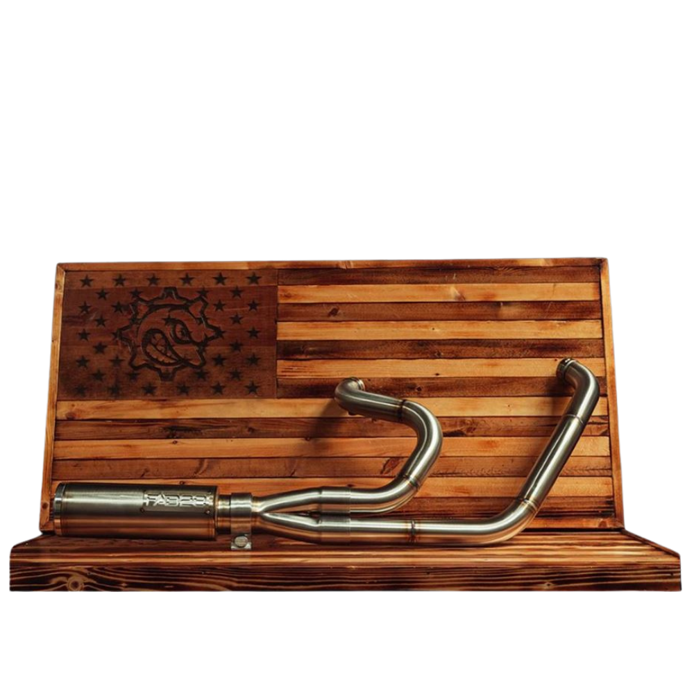 The Fab 28 Stainless Exhaust for 1999-2017 Harley-Davidson Dyna is mounted on a wooden American flag display, showcasing a bold dragon design burned into the wood.