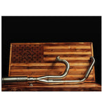 The Fab 28 Stainless Exhaust for 2017-Up Harley-Davidson Touring is shown in front of a wooden American flag with a bull design engraved on the blue field.
