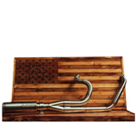 The Fab 28 Stainless Exhaust for 2017-Up Harley-Davidson Touring is shown in front of a wooden American flag with a bull design engraved on the blue field.