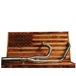 The Fab 28 Stainless Exhaust for 2017-Up Harley-Davidson Touring is shown in front of a wooden American flag with a bull design engraved on the blue field.