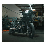 The Fab 28 Stainless Exhaust for 2018-Up Harley-Davidson Softail by Fab 28 is shown in front of a wooden American flag featuring a horse design, ideal for Harley-Davidson Softail enthusiasts.