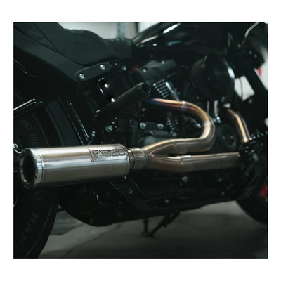 The Fab 28 Stainless Exhaust with Canister Muffler For Harley '18+ M8 Softail is showcased in front of a wooden panel that features a carved American flag and a design incorporating pipes and gears, echoing the craftsmanship found on a Harley M8 Softail.