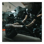 The Fab 28 Stainless Exhaust for 2018-Up Harley-Davidson Softail by Fab 28 is shown in front of a wooden American flag featuring a horse design, ideal for Harley-Davidson Softail enthusiasts.