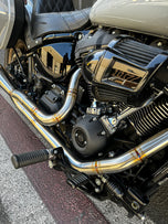 Close-up of a Harley Davidson M8 Softail highlighting the rear wheel, brake disc, and an SP Concepts Mid Length Elsinore Exhaust with a sleek metallic finish and logo.