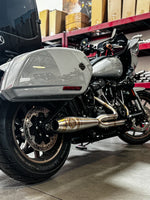 Close-up of a Harley Davidson M8 Softail highlighting the rear wheel, brake disc, and an SP Concepts Mid Length Elsinore Exhaust with a sleek metallic finish and logo.
