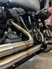 Close-up of a Harley Davidson M8 Softail highlighting the rear wheel, brake disc, and an SP Concepts Mid Length Elsinore Exhaust with a sleek metallic finish and logo.