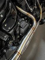 Close-up of a Harley Davidson M8 Softail highlighting the rear wheel, brake disc, and an SP Concepts Mid Length Elsinore Exhaust with a sleek metallic finish and logo.