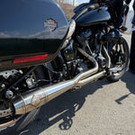 A sleek black Harley Davidson M8 Softail with an SP Concepts Works Edition Mid Length Elsinore Exhaust gleams under the sun on a concrete surface. Featuring saddlebags and a distinctive logo, this motorcycle exudes style and power.