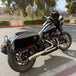 A sleek black Harley Davidson M8 Softail with an SP Concepts Works Edition Mid Length Elsinore Exhaust gleams under the sun on a concrete surface. Featuring saddlebags and a distinctive logo, this motorcycle exudes style and power.
