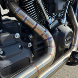 A sleek black Harley Davidson M8 Softail with an SP Concepts Works Edition Mid Length Elsinore Exhaust gleams under the sun on a concrete surface. Featuring saddlebags and a distinctive logo, this motorcycle exudes style and power.