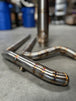 In a workshop with polished metal exhaust pipes, a worker, and an American flag above, the SP Concepts Works Edition Mid Length Elsinore Exhaust for Harley Davidson M8 Touring Bagger 2017-Up is showcased as ideal for enhancing performance.