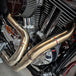 A SP Concepts stainless steel header with multiple bends rests on a gray surface, highlighting its craftsmanship. In the background, an American flag-designed welding mask nods to the customization spirit of Harley Davidson Sportster and Lanesplitter Exhaust fans.