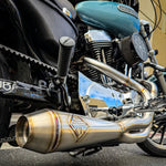 A SP Concepts stainless steel header with multiple bends rests on a gray surface, highlighting its craftsmanship. In the background, an American flag-designed welding mask nods to the customization spirit of Harley Davidson Sportster and Lanesplitter Exhaust fans.