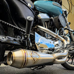 A SP Concepts stainless steel header with multiple bends rests on a gray surface, highlighting its craftsmanship. In the background, an American flag-designed welding mask nods to the customization spirit of Harley Davidson Sportster and Lanesplitter Exhaust fans.