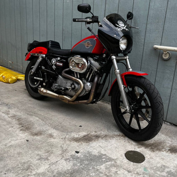 An SP Concepts Lanesplitter Exhaust for Harley Davidson Sportster (1986-2003) is showcased on a textured surface with intricate curves. Nearby, an American flag-patterned helmet hints at the increased torque this meticulously welded stainless steel product promises.