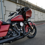 A red Harley-Davidson touring motorcycle equipped with an Arlen Ness Big Sucker Stage 1 Air Cleaner is parked on a street beside a concrete wall topped with a metal fence.