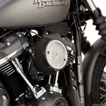 A red Harley-Davidson touring motorcycle equipped with an Arlen Ness Big Sucker Stage 1 Air Cleaner is parked on a street beside a concrete wall topped with a metal fence.