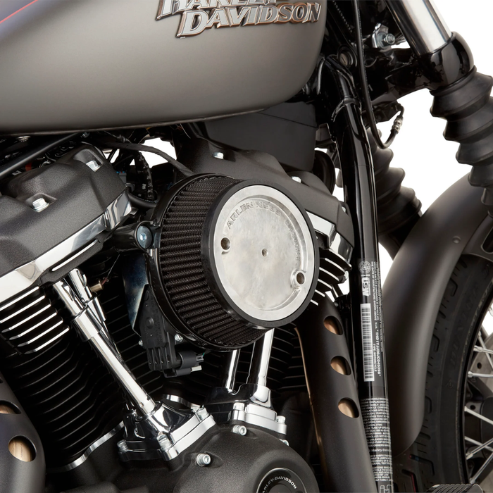 A red Harley-Davidson touring motorcycle equipped with an Arlen Ness Big Sucker Stage 1 Air Cleaner is parked on a street beside a concrete wall topped with a metal fence.